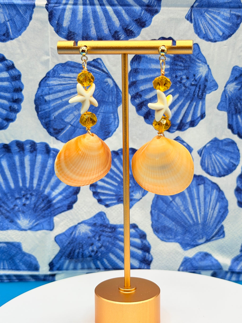 Pair of golden cockle shell earrings on white display stand showing both shells and full drop