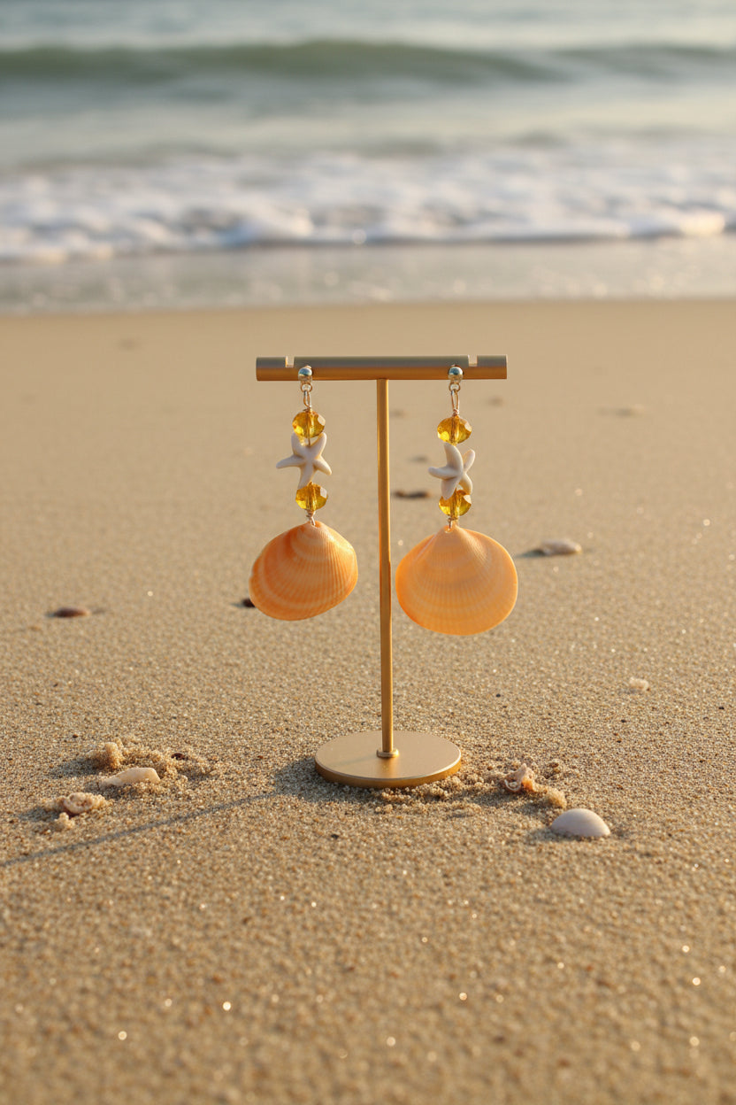 Single golden cockle shell earring on white background showing starfish charm and amber crystal bead detail close-up