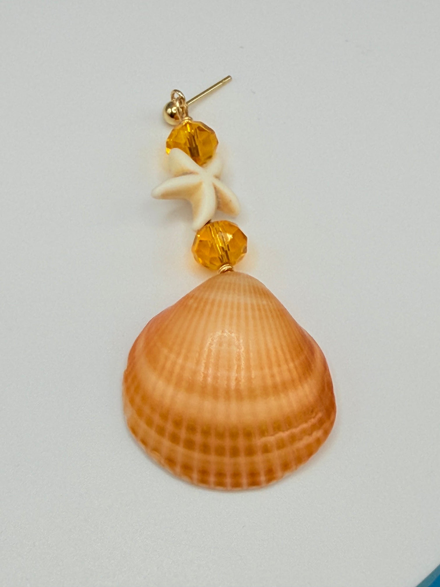 Single golden cockle shell earring on white background showing front of shell smooth peach tone
