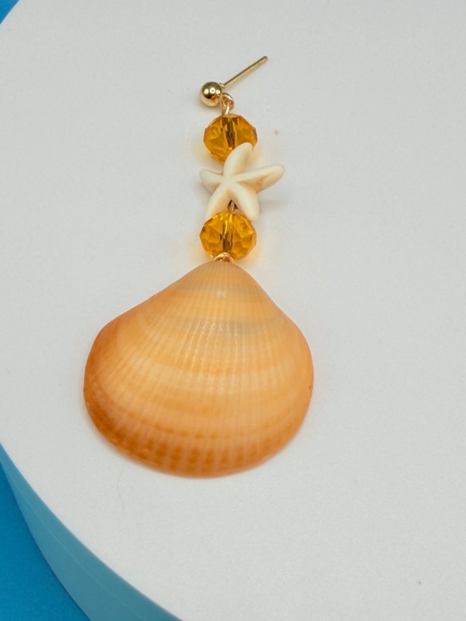 Single golden cockle shell earring on white background showing side profile and full drop
