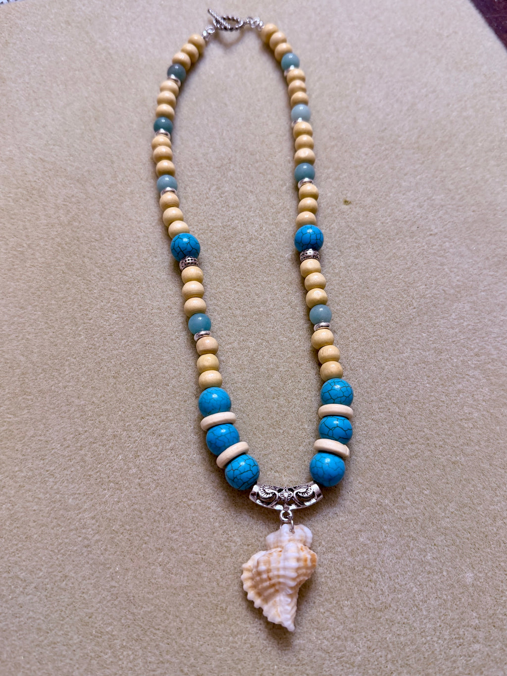 Turquoise beaded conch shell necklace laid on driftwood by the shore