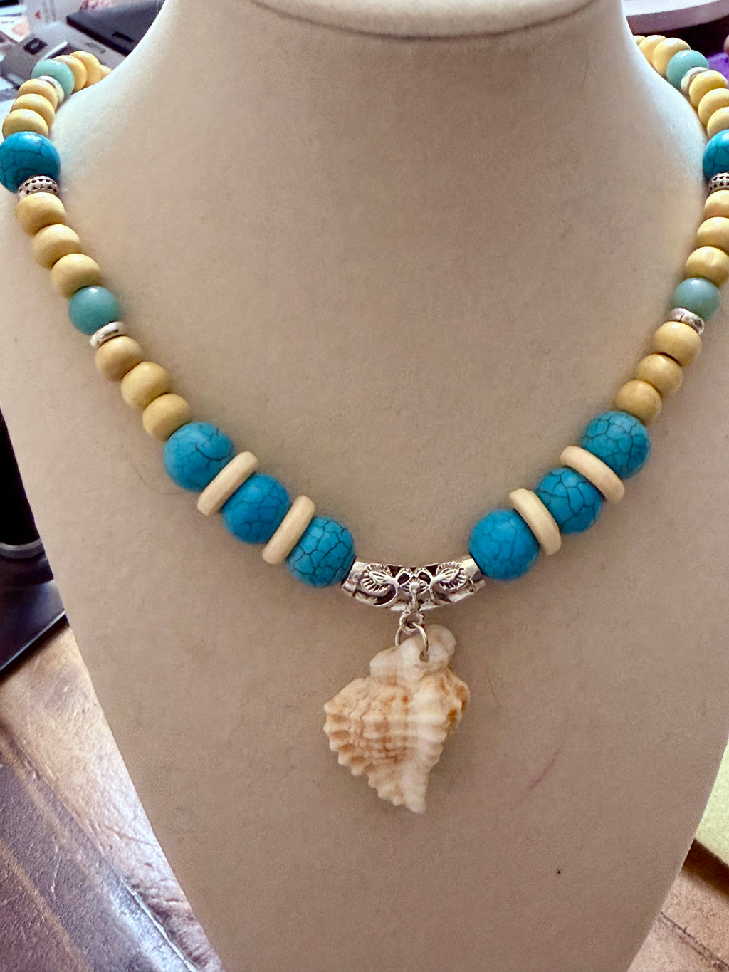Turquoise and sand-toned beaded necklace with conch shell pendant on beach sand