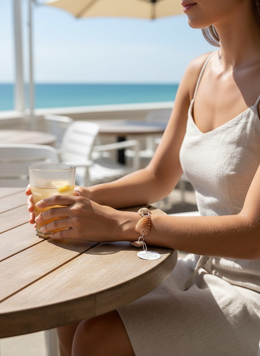 Shoreline Keepsakes cardita shell bracelet with silver links worn by a woman at a beachside table.