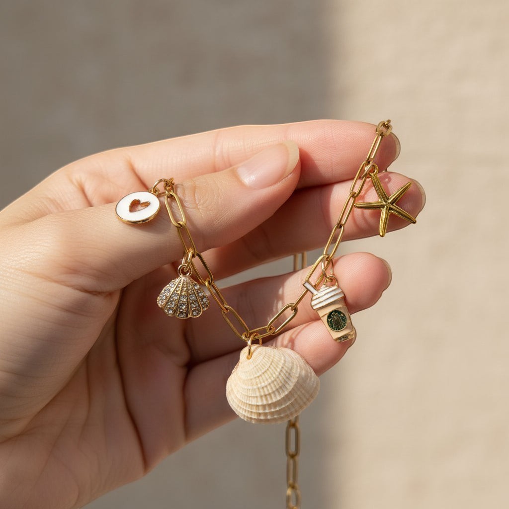 Shoreline Keepsakes gold paperclip chain bracelet with a ribbed venus clam shell, starfish, and iced coffee charm.
