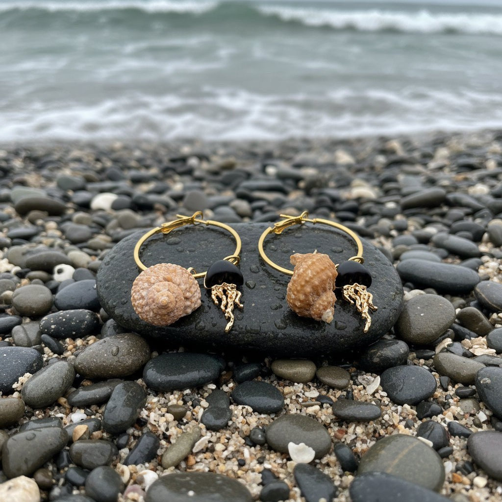 Shoreline Keepsakes gold hoop earrings with turban shells, matte black beads, and jellyfish charms on a beach stone.